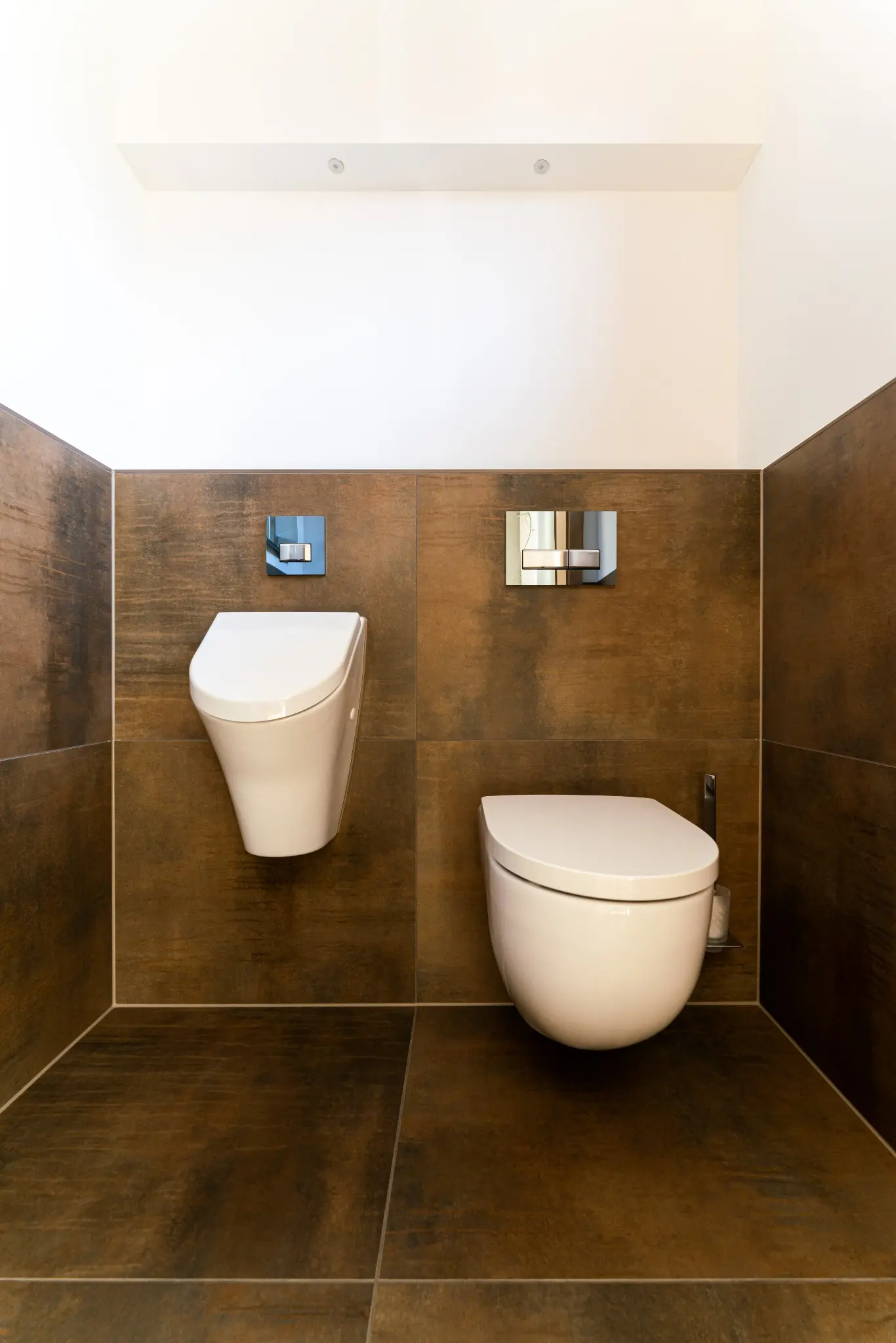 WC und Urinal vor symmetrisch eingeteilten Fliesen in Rostoptik